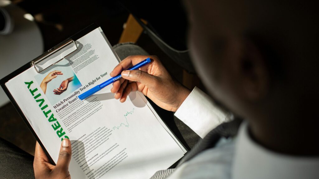 A person in a suit analyzing a document about creativity on a clipboard, using a blue pen.